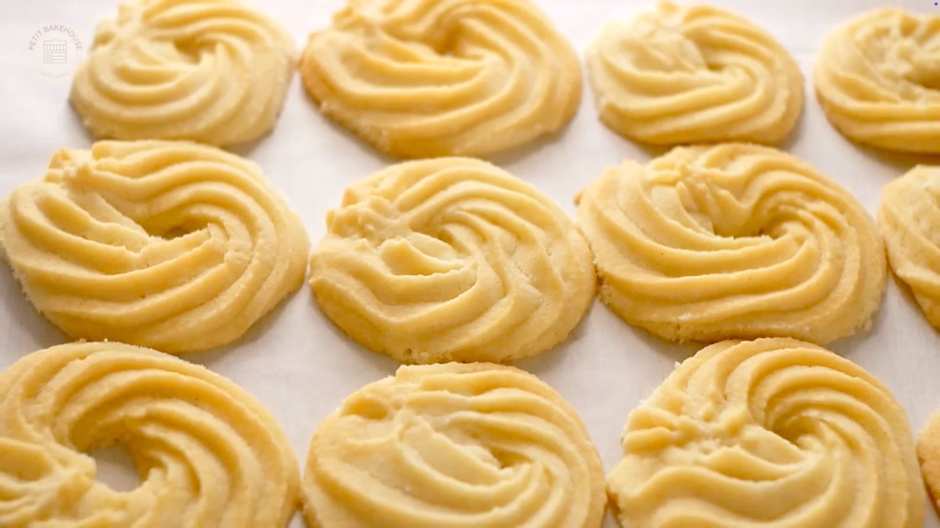 Golden-baked butter shortbread cookie rings neatly arranged on a baking tray, lightly dusted with powdered sugar.