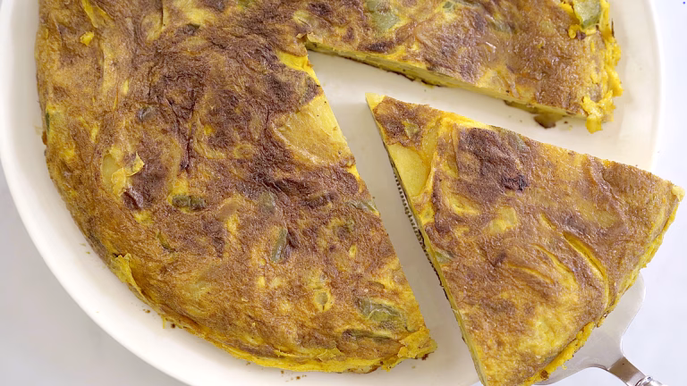 Spanish omelette recipe slice lifted from a plate, showing golden crust and potato layers